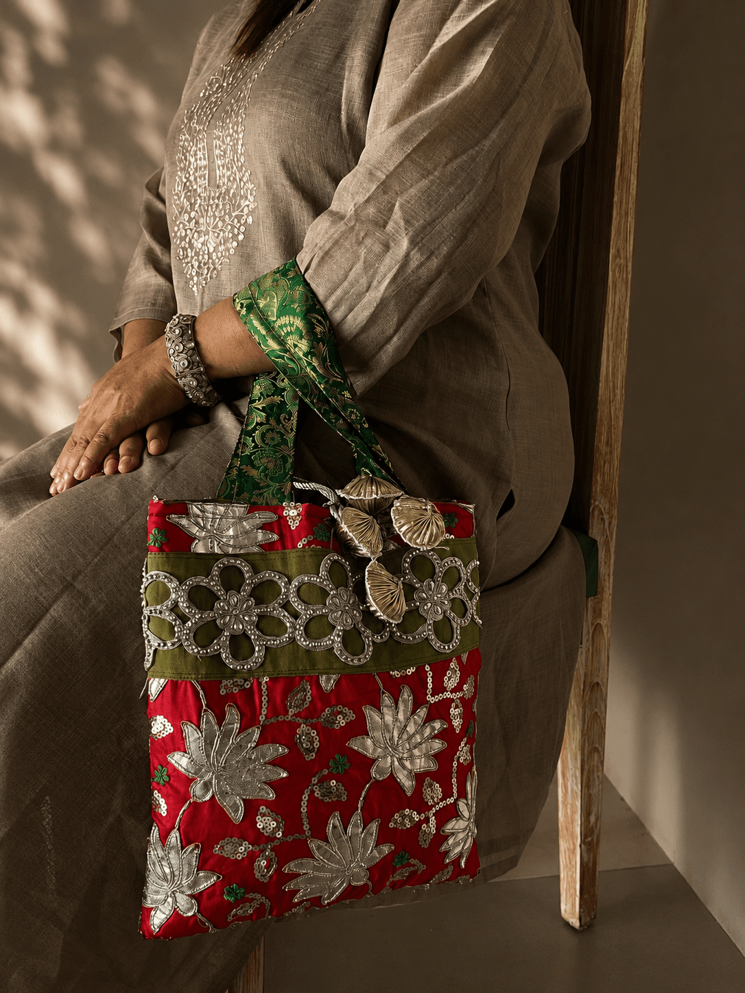 Red embroidered tote bag with silver floral appliqué held by a woman